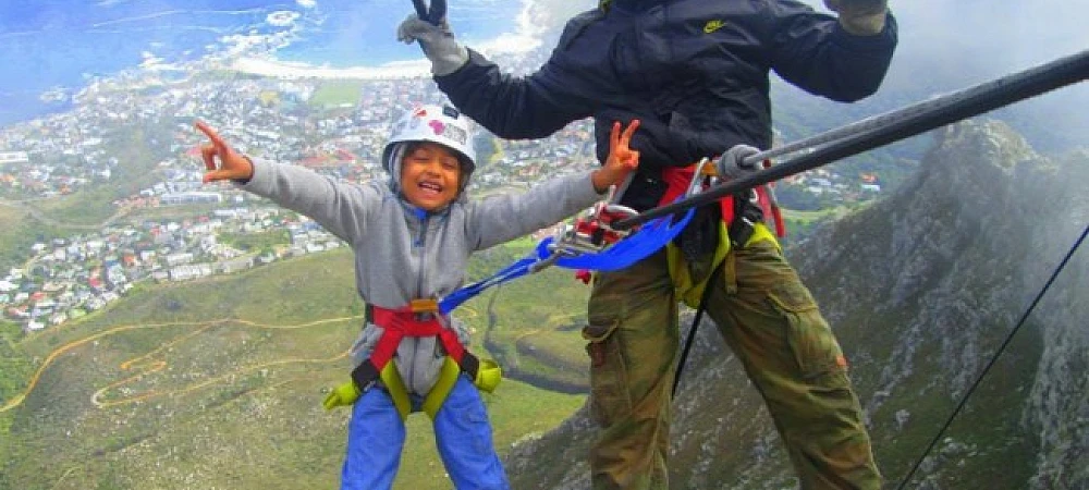 Man and child secured by ropes, smiling and throwing peace signs with a townscape in the background.